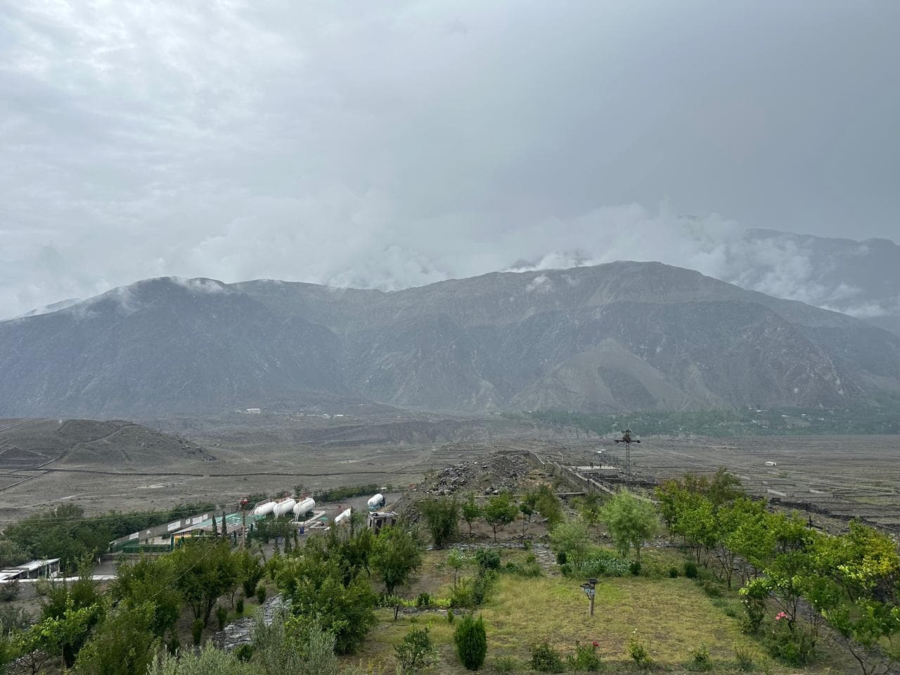 The Gitco Gas LPG plant on the valley floor in Gilgit-Baltistan, with cloud-covered mountains rising behind it.